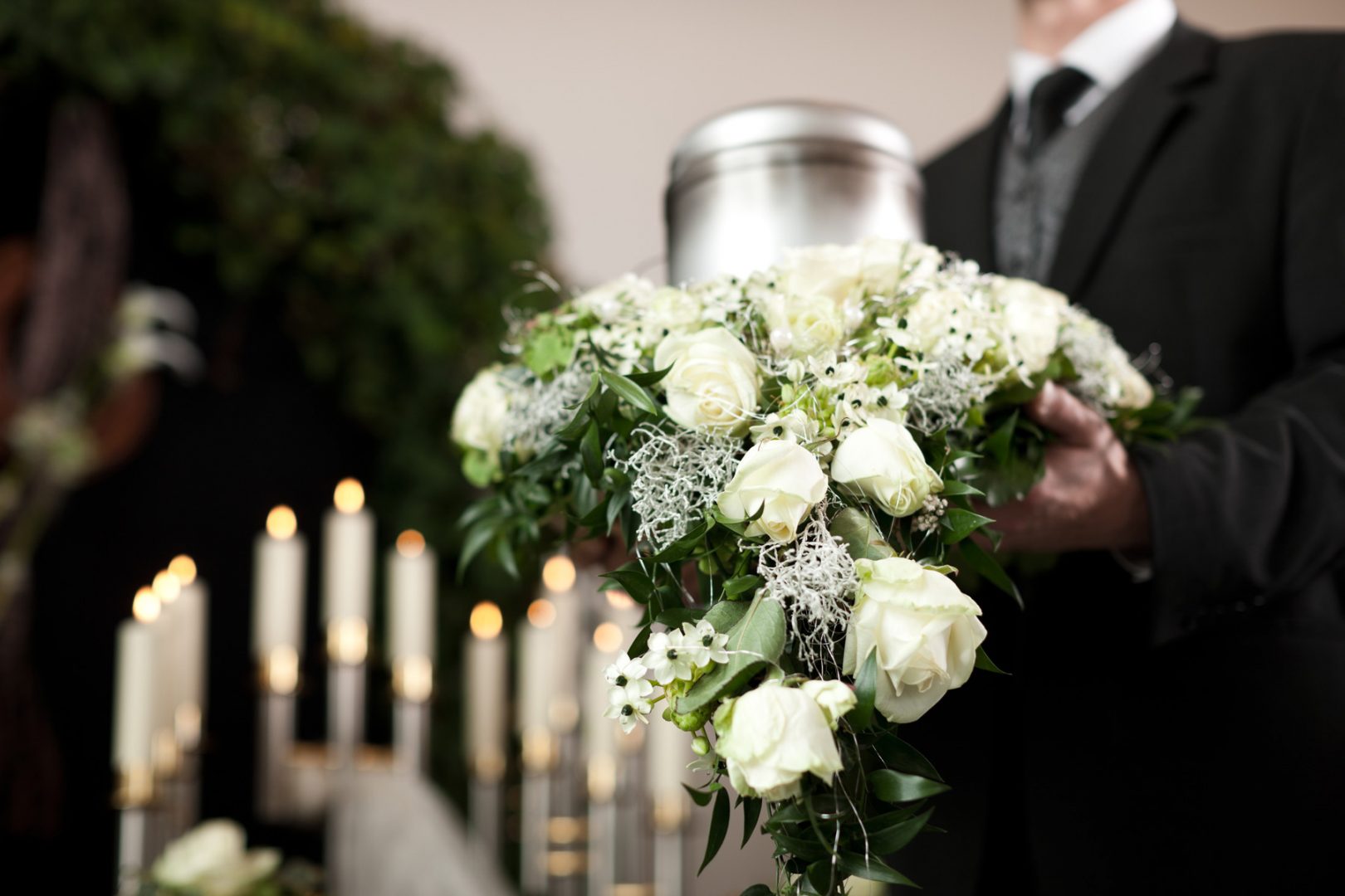 Bestatter hält Urne mit Blumenschmuck